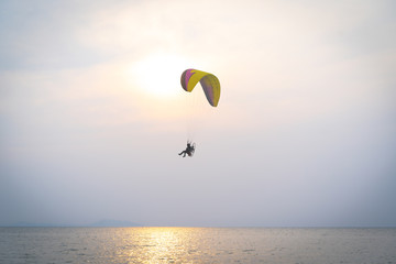 A man is flying with a powered parachute over the beach in Thailand.