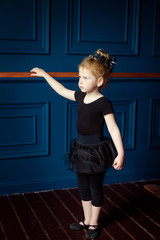 View of little blonde curly ballerina in black leotard practicing at ballet barre stand one at dance studio. Kids hobby dancing. Ballet is hard work for children. Active lifestyle in childhood
