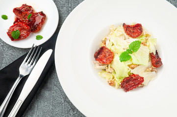 Salad with sun-dried tomatoes, Peking cabbage, walnuts and Parmesan cheese. On a white plate. Near the fork and knife. View from above. On a gray concrete background.