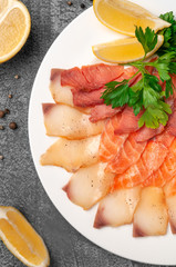 Fish platter salmon and oily fish. On a large white plate. Garnished with a slice of lemon and herbs. View from above. On a gray concrete background.