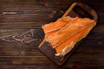 Hot smoked salmon trim and leftovers with bones and fins on dark wooden background.