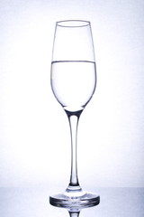 isolated glass goblet with liquid on mirror surface, backlight, portrait orientation