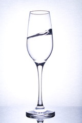 isolated glass goblet with waved liquid, mirror surface, backlight, portrait orientation