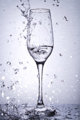 isolated glass goblet with liquid in it, on mirror surface, backlight, portrait orientation, water splashes