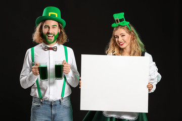 Young couple with blank poster and beer on dark background. St. Patrick's Day celebration