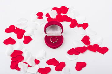 Red velvet heart shaped ring box with engagement ring inside among fabric red and white hearts. Gift for valentines day, birthday. Marriage proposal concept. Close up