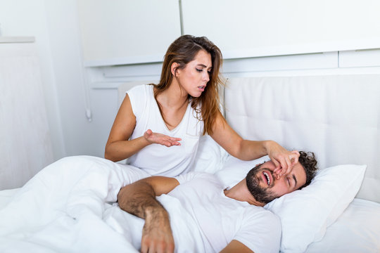 Couple in bed, man snoring and woman can't sleep. Snoring man and young woman. Couple sleeping in bed. Young girl can't sleep because of her man's snoring holding his nose. Snoring man problem