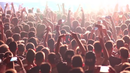 Fans waving their hands and filming by phones crowd at a concert partying at a night club with DJ performing on stage
