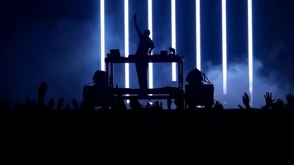 Silhouettes of DJ playing favorite music and exalted crowd attending a concert back lit by stage lights, raised hands and cheering crowd 