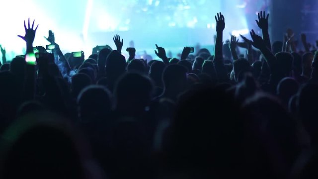 Music concert on stage and crowd clapping in the audience, cheering group of people in silhouette applauding a rock band 