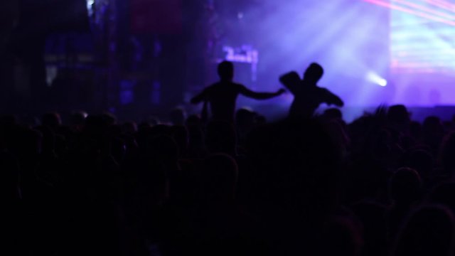 Silhouettes of young people jumping and raising hands at music concert, taking off t-shirts over exalted crowd applause  