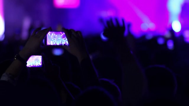 People at music rock concert taking photos or recording video with smartphones, party crowd cheering at music event with flashing light show
