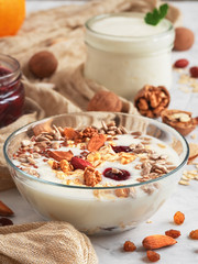 Yogurt with granola and nuts in a glass cup on a gray stone table background. Ingredients for breakfast on the table. Selective focus, shallow depth of field. Close-up. Vertical orientation.