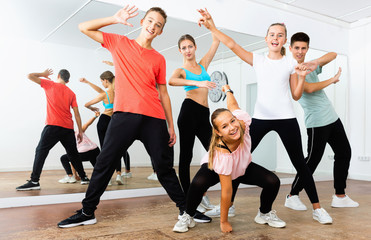 Cheerful teenage boys and girls having fun in choreography class, posing with female trainer