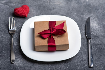 Gift box with red ribbon on a white plate. Creative holiday concept