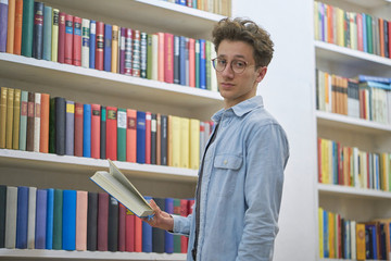 Teenager with glasses in library looking into the camera.