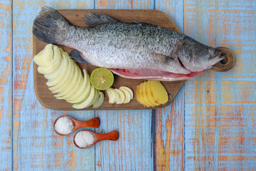 Barramundi or asian seabass fish with salt, msg,ginger,garlic,onion, , and key lime over the wooden cutting board.