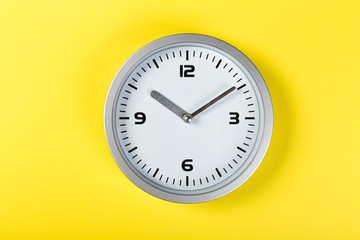 White wall clock with a yellow used hanging on the wall. Minimalist image of a wall clock on a yellow background with copy space