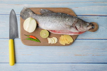 Barramundi or asian seabass fish with knife, chilies, onion ,ginger,garlic,and key lime over the wooden cutting board.