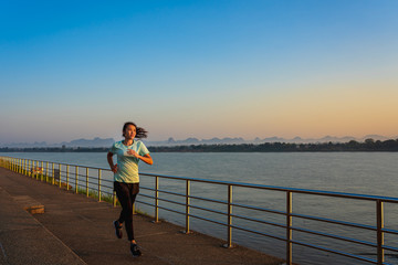 Young fitness Asian woman is running and jogging an outdoor workout on the riverwalk in the morning for lifestyle health.