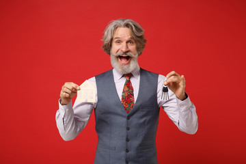 Excited elderly gray-haired mustache bearded man in classic shirt vest and colorful tie isolated on red wall background. People lifestyle concept. Mock up copy space. Holding house and bunch of keys.