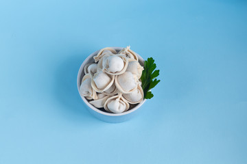 Raw, frozen dumplings in a blue bowl on a light background. With parsley leaves and allspice beans.