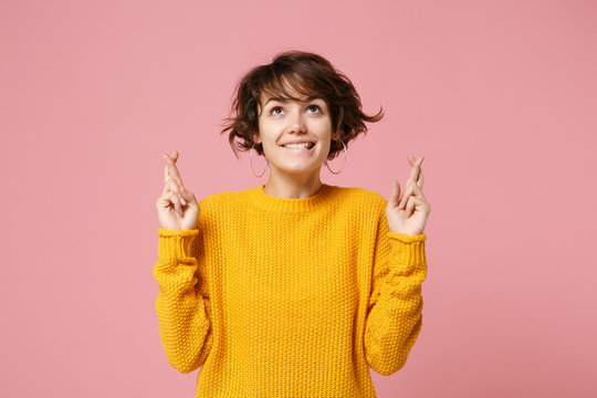 Pretty young brunette woman in yellow sweater posing isolated on pastel pink background. People lifestyle concept. Mock up copy space. Waiting for special moment, keeping fingers crossed, making wish.