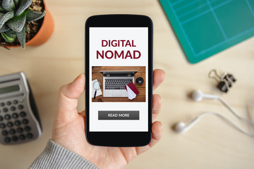 Hand holding smart phone with digital nomad concept on screen. Top view
