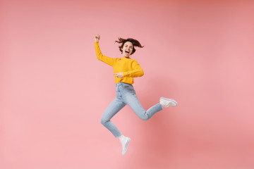 Fototapeta na wymiar Excited young brunette woman girl in yellow sweater posing isolated on pastel pink background in studio. People lifestyle concept. Mock up copy space. Having fun fooling around, rising hands, jumping.