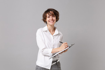 Smiling young business woman in white shirt posing isolated on grey wall background. Achievement...