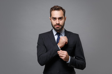 Successful young business man in classic black suit shirt tie posing isolated on grey background studio portrait. Achievement career wealth business concept. Mock up copy space. Straightening sleeves.