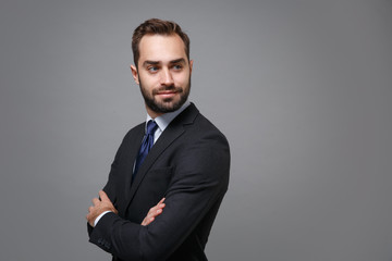 Side view of young business man in classic black suit shirt tie posing isolated on grey background. Achievement career wealth business concept. Mock up copy space. Holding hands crossed looking aside.