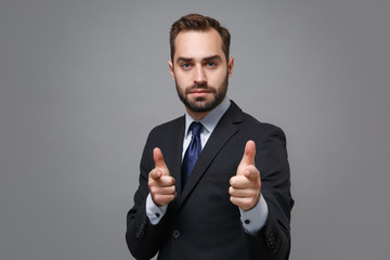 Handsome young business man in classic black suit shirt tie posing isolated on grey background in studio. Achievement career wealth business concept. Mock up copy space. Point index fingers on camera.