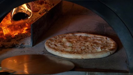 Italian pizza with 4 cheeses is cooked in the oven, restaurant chef takes pizza out of a wood fired oven at restaurant.