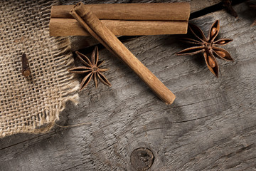 Old wooden plank background with cinnamon sticks, anise star, cloves in border. Natural spice frame with copy space.