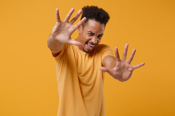 Scared young african american guy in casual t-shirt posing isolated on yellow orange wall background studio portrait. People lifestyle concept. Mock up copy space. Screaming, covering with hands.