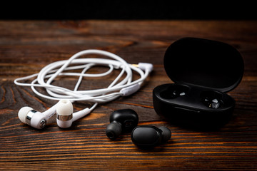 Black wireless and white wired headphones on dark wooden background.