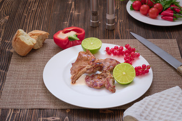 Grilled lamb steak on a white plate. Dark wood wooden table. Vegetables and spices on the table
