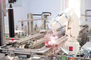 Focus on robot arm's gripper. Industry 4.0 concept; artificial intelligence in smart factory. Robot picks up the product from automated car on the manufacturing line. Selective focus.