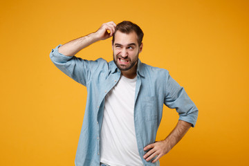 Preoccupied young bearded man in casual blue shirt posing isolated on yellow orange background...