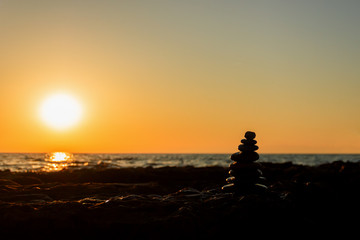Silhouette of a pyramid of stones for meditation, lying on the sea coast at sunset, in the contoured light of the sun. Low key photography