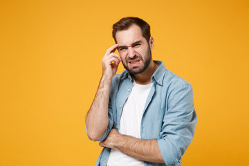 Preoccupied puzzled young bearded man in casual blue shirt posing isolated on yellow orange background, studio portrait. People emotions lifestyle concept. Mock up copy space. Putting hand on head.