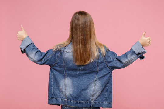 Back Rear View Of Little Blonde Kid Girl 12-13 Years Old In Denim Jacket Isolated On Pastel Pink Wall Background Children Portrait. Childhood Lifestyle Concept. Mock Up Copy Space. Showing Thumbs Up.