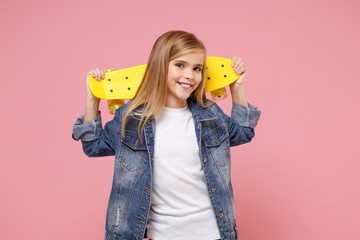 Smiling little blonde kid girl 12-13 years old in denim jacket posing isolated on pastel pink background children portrait. Childhood lifestyle concept. Mock up copy space. Hold yellow skateboard. © ViDi Studio