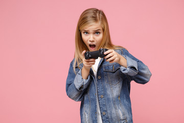 Shocked little blonde kid girl 12-13 years old in denim jacket posing isolated on pastel pink background children portrait. Childhood lifestyle concept. Mock up copy space. Play game with joystick.