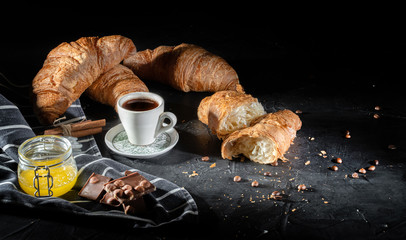 Freshly baked croissants and cup of coffe on dark background. Perfect breacfast in the morning