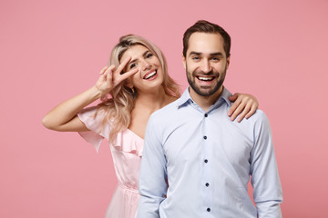 Cheerful young couple two guy girl in party outfit celebrating posing isolated on pastel pink background. People lifestyle Valentine's Day Women's Day birthday holiday concept. Showing victory sign.