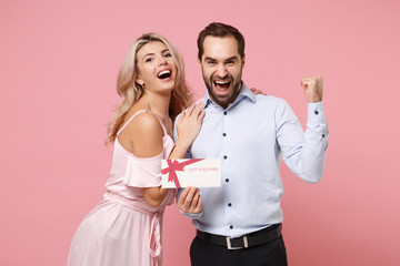 Young couple two guy girl in party outfit celebrating posing isolated on pastel pink background. Valentine's Day, Women's Day birthday holiday concept. Hold gift certificate, doing winner gesture.