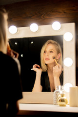 blonde woman in dress near makeup mirror