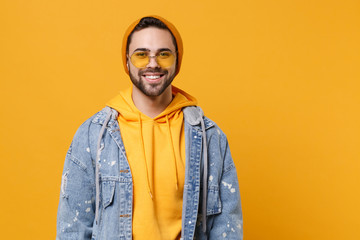 Smiling young hipster guy in fashion jeans denim clothes posing isolated on yellow orange background studio portrait. People sincere emotions lifestyle concept. Mock up copy space. Looking camera.